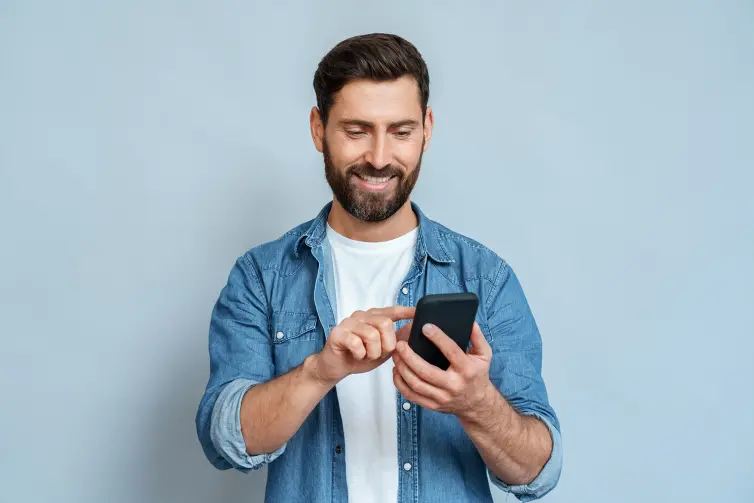 Smiling man using smartphone standing isolated on blue background copy space.