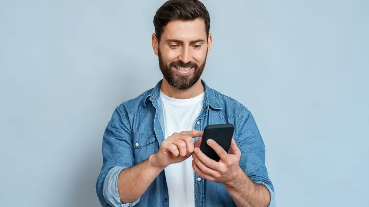 Smiling man using smartphone standing isolated on blue background copy space.