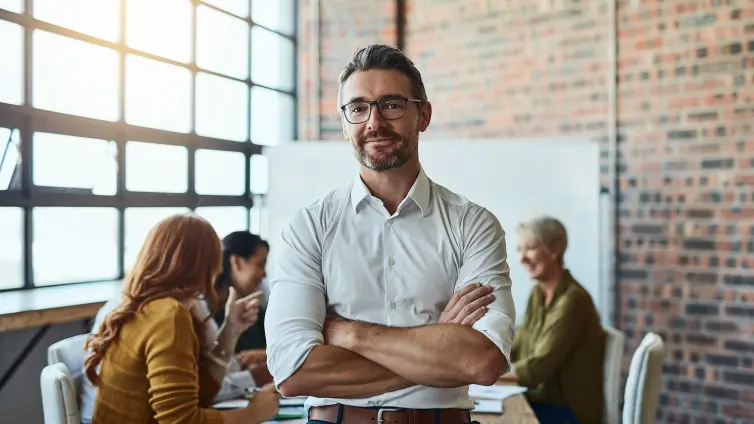 Man sat on edge of table, with people sat at the table behind him.