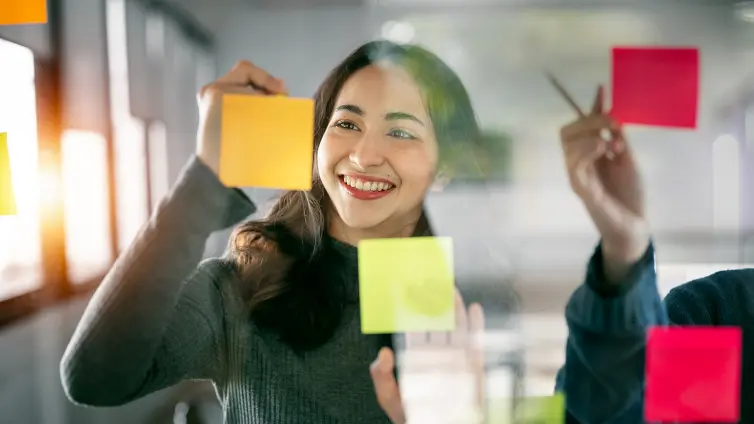 Woman writing on a post-it note stuck on a glass wall.