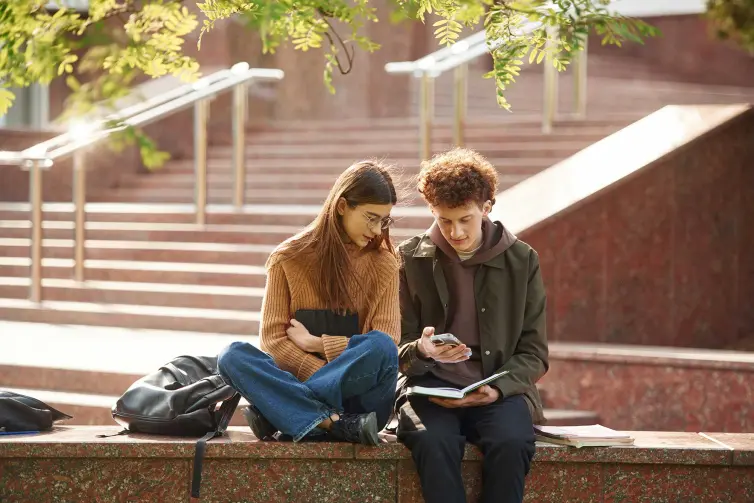Sitting together. Man and woman students are outdoors near university.